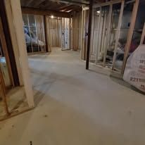 Interior view of a room under construction with wooden studs and concrete floor.