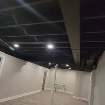 Basement with black ceiling, recessed lights, and white walls; a metal bar extends to the ceiling.