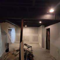 Black ceiling with exposed beams, white walls, unfinished room.