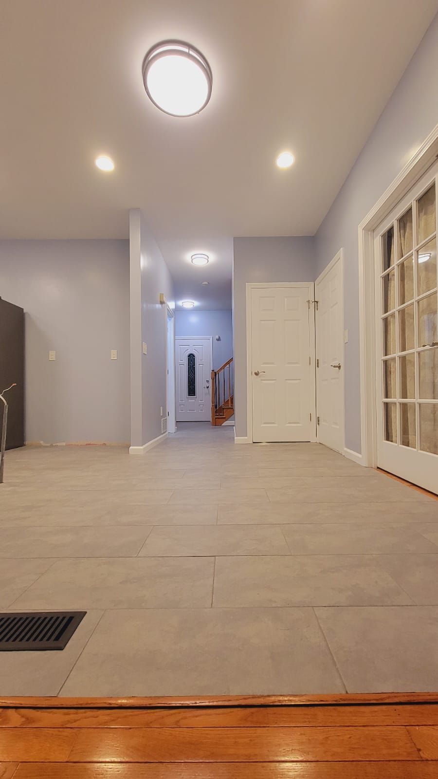 Empty room with light gray floors, pale blue walls, and a hallway leading to a staircase.