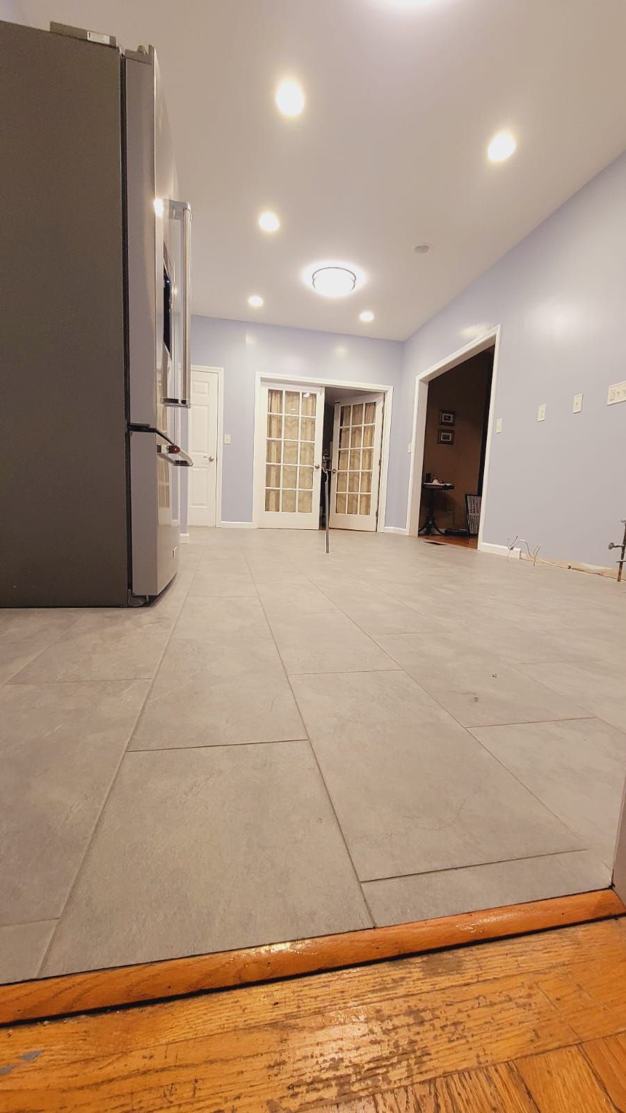 Gray tiled kitchen floor with a refrigerator and French doors in the background.