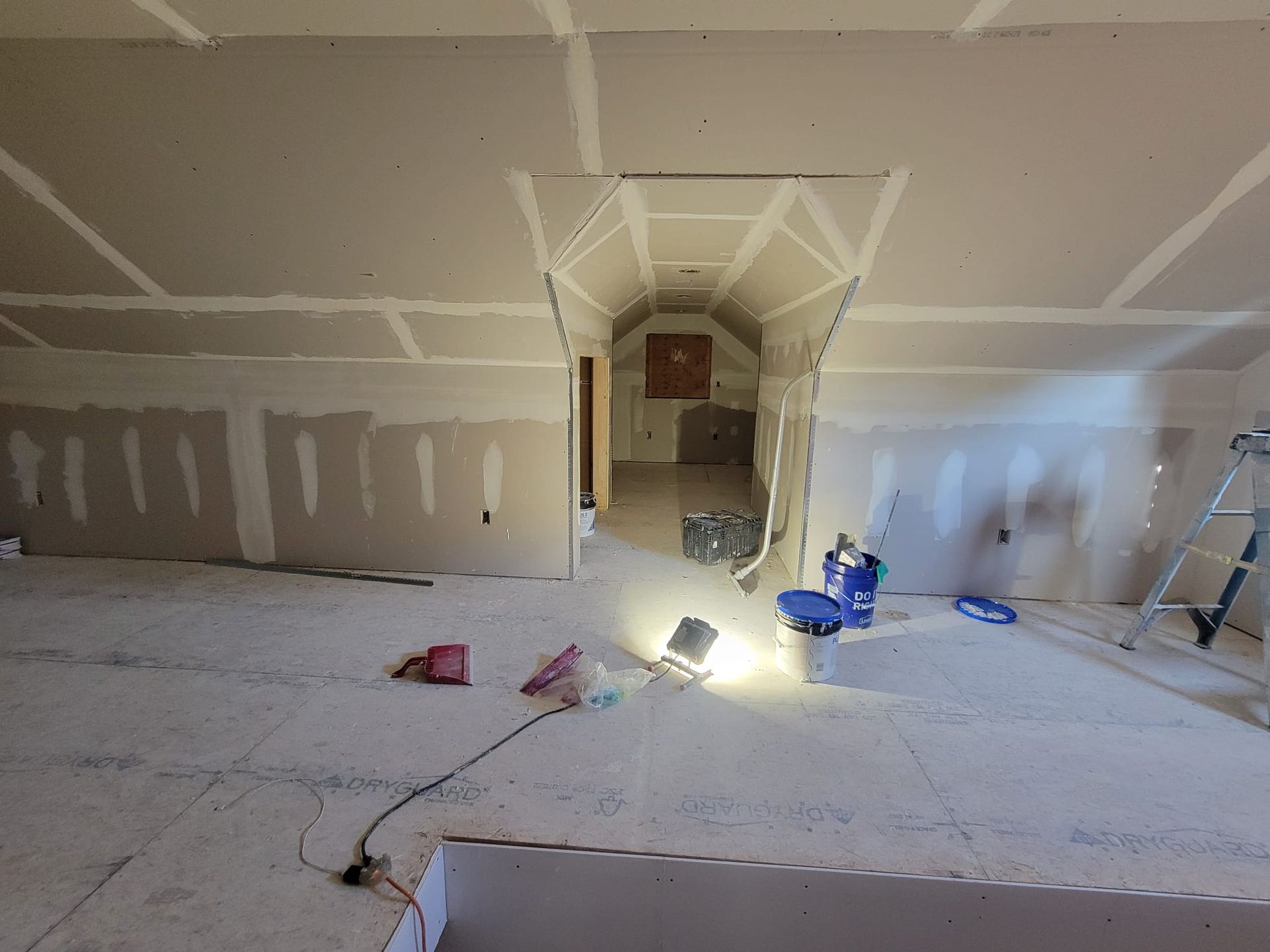 Interior construction site with drywall; open space, unfinished walls and ceiling, bright work lights.