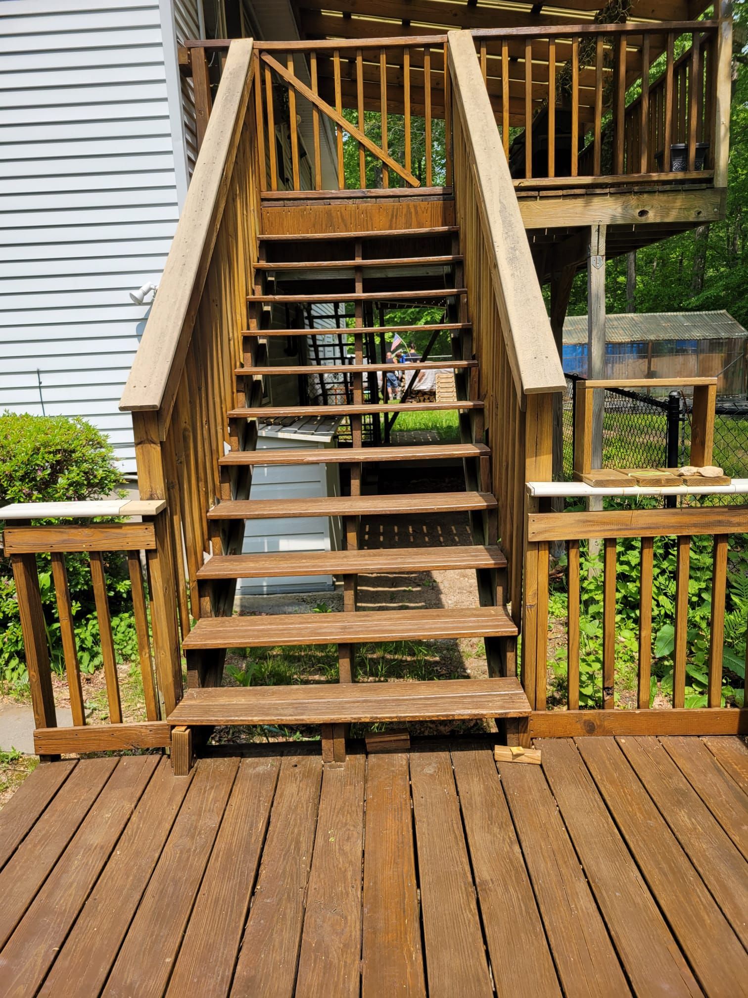 Wooden outdoor staircase leading up to a deck; stained brown; railings on both sides.
