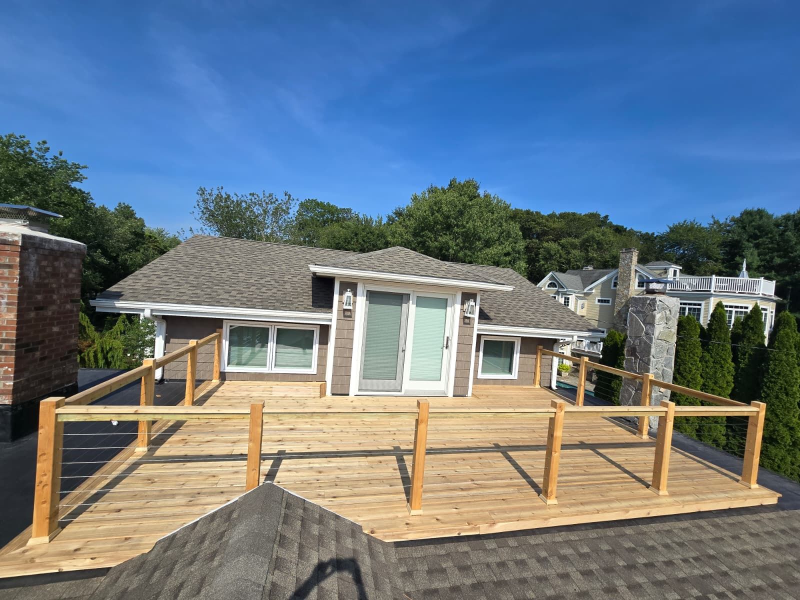 A rooftop deck with wooden railings surrounds a house with a light brown exterior.