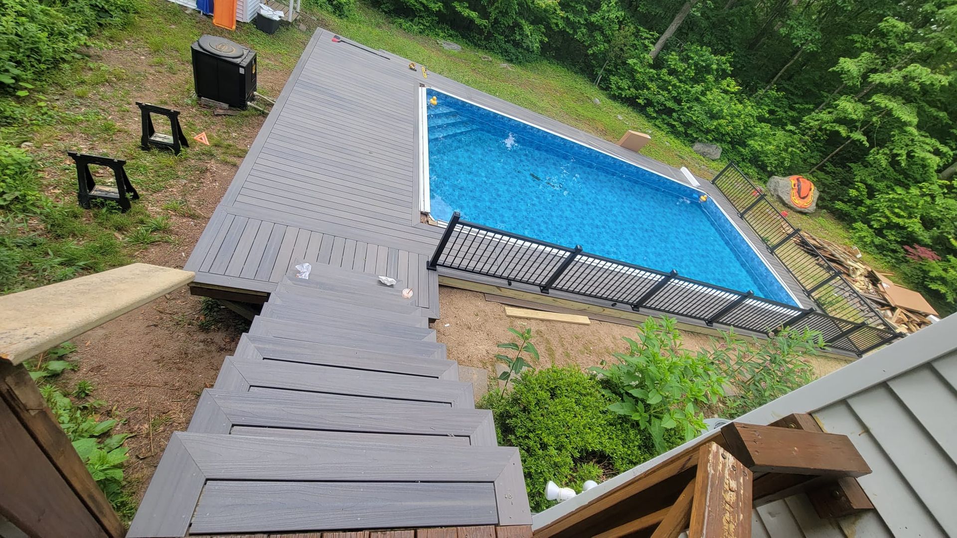 Above view of a rectangular pool with a deck and stairs in a wooded area. Grey deck and stairs.