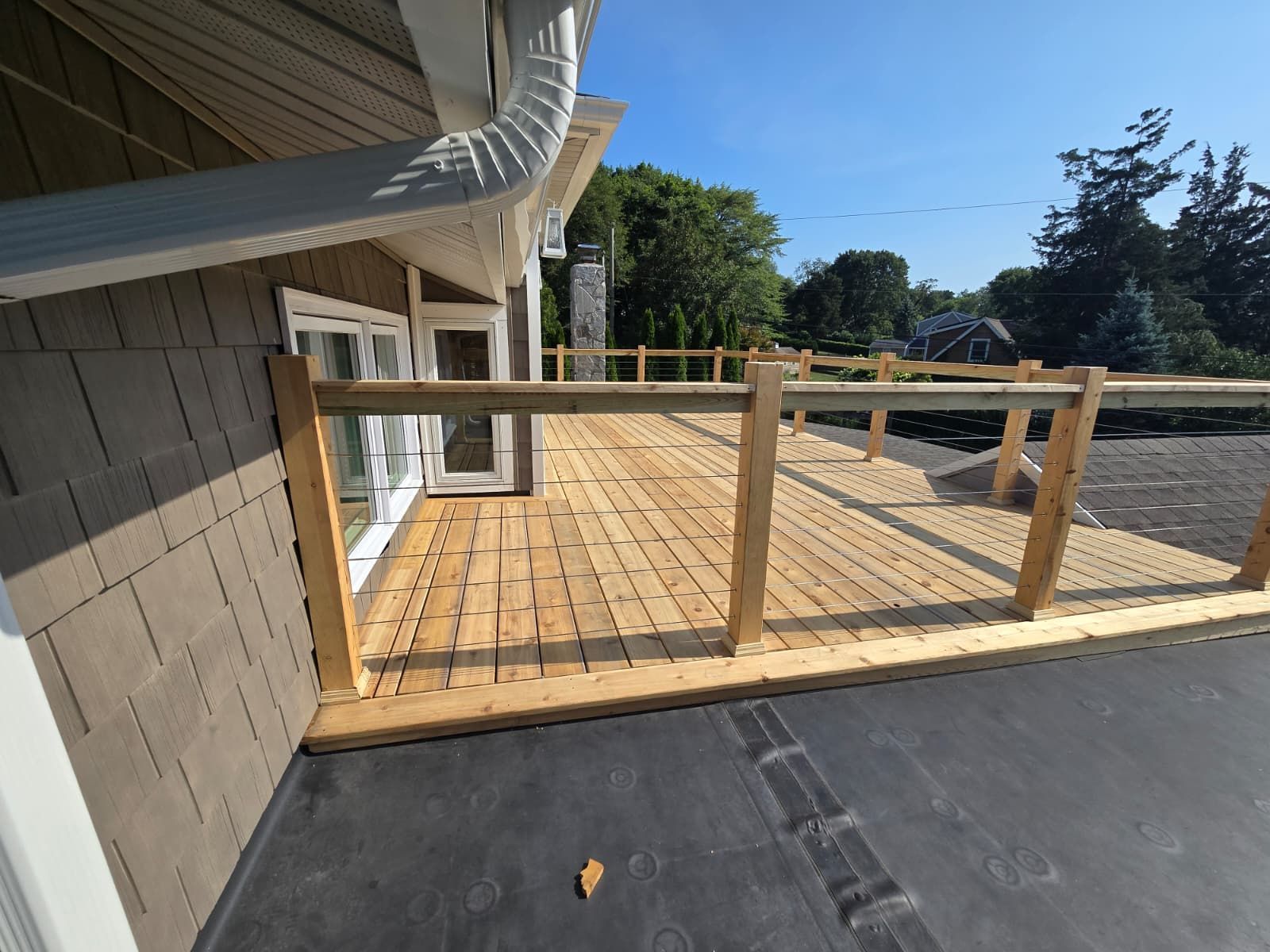 Wooden deck with glass railing attached to a house with brown siding, sunny day.