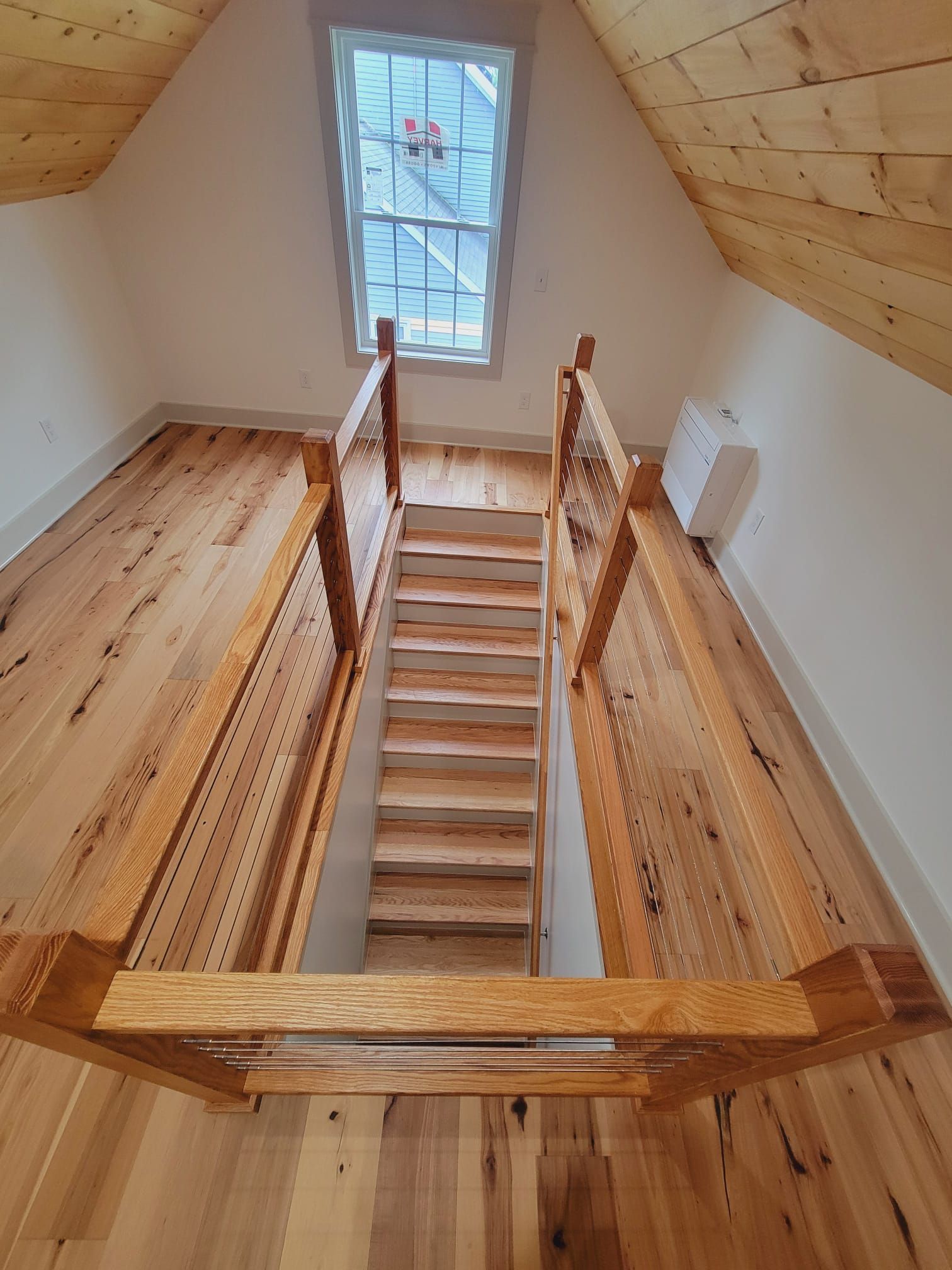 Wooden staircase leading to an attic room with a window and hardwood flooring.