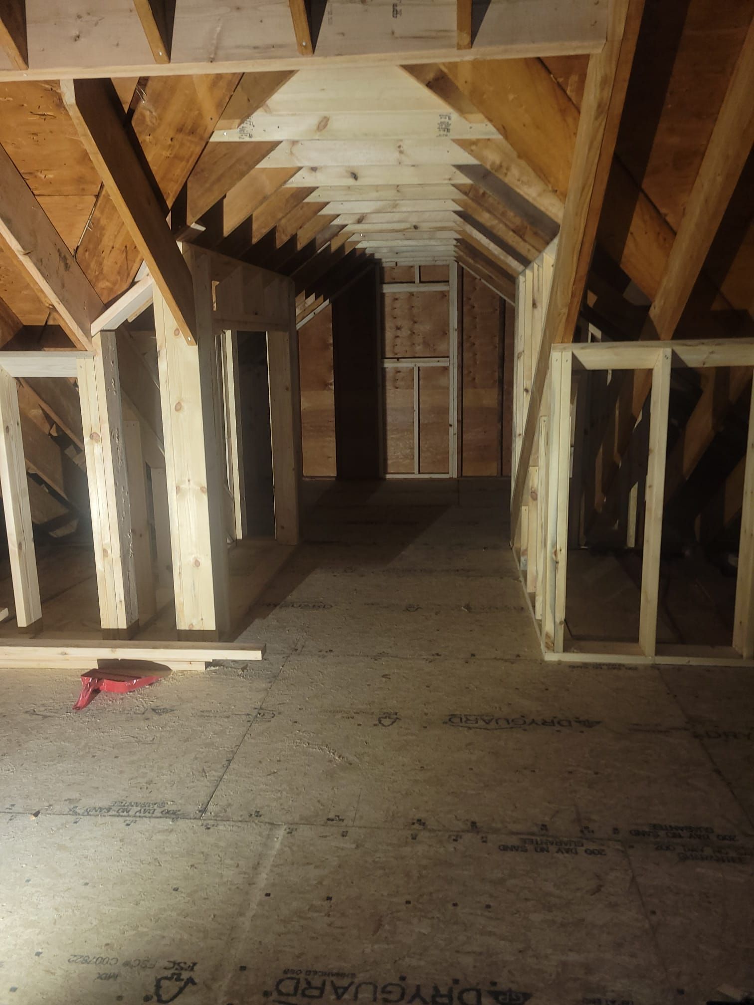 Interior view of an unfinished attic with exposed wooden beams and studs, a door in the distance.
