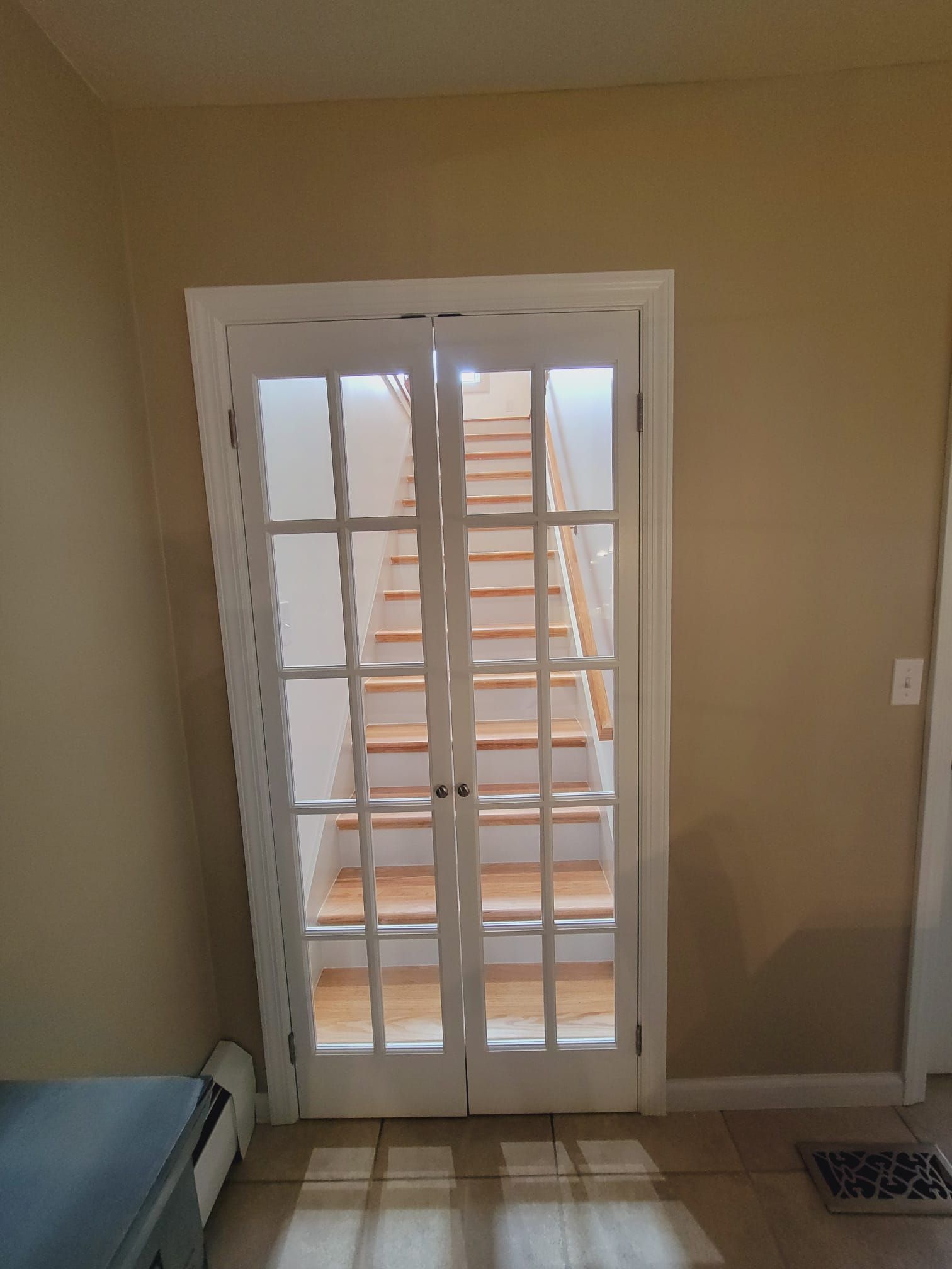 White French doors open to a wooden staircase. Beige walls surround the doors, a radiator is visible on the left.