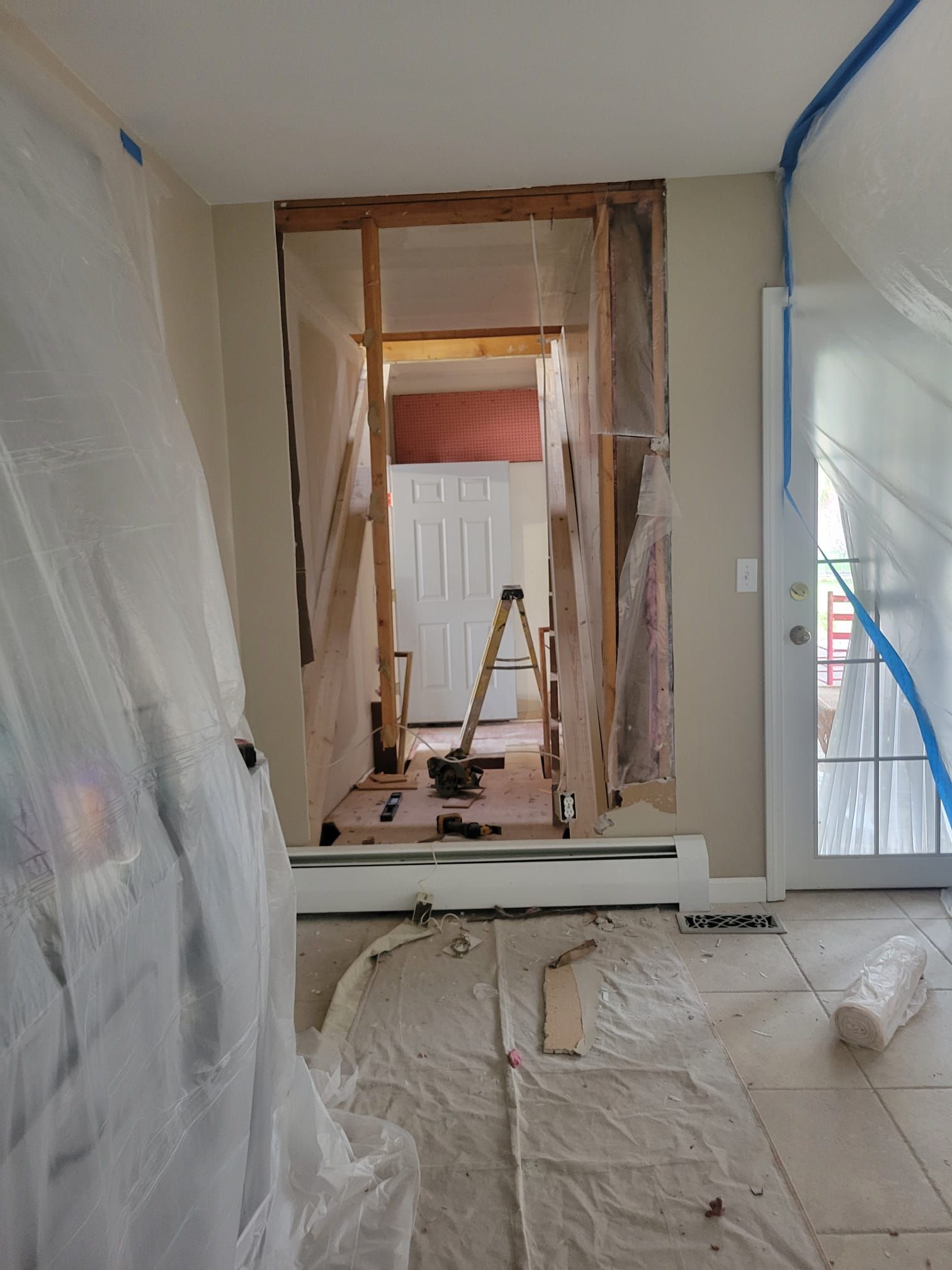 Interior doorway under construction, covered in plastic sheeting. White walls, exposed wood framing, and ladder.