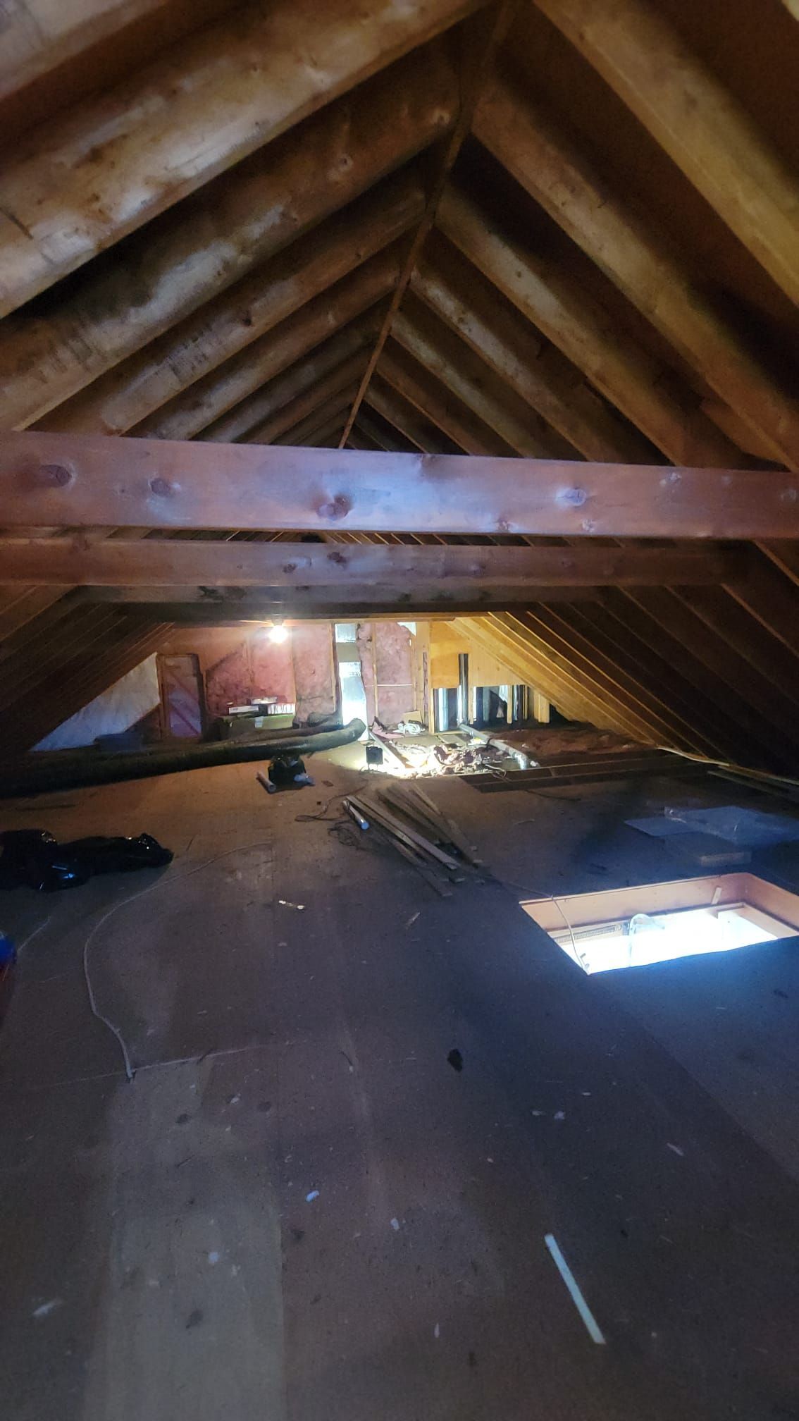 Attic interior with wooden beams.  Dark, unfinished space with debris on floor and light from openings.