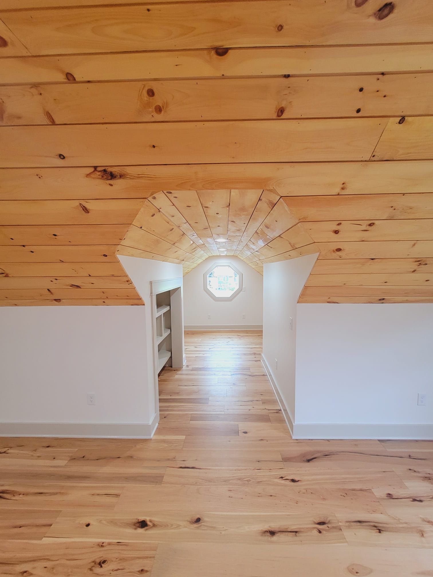 Interior view: Wood ceiling and floor, white walls, small room with octagonal window.