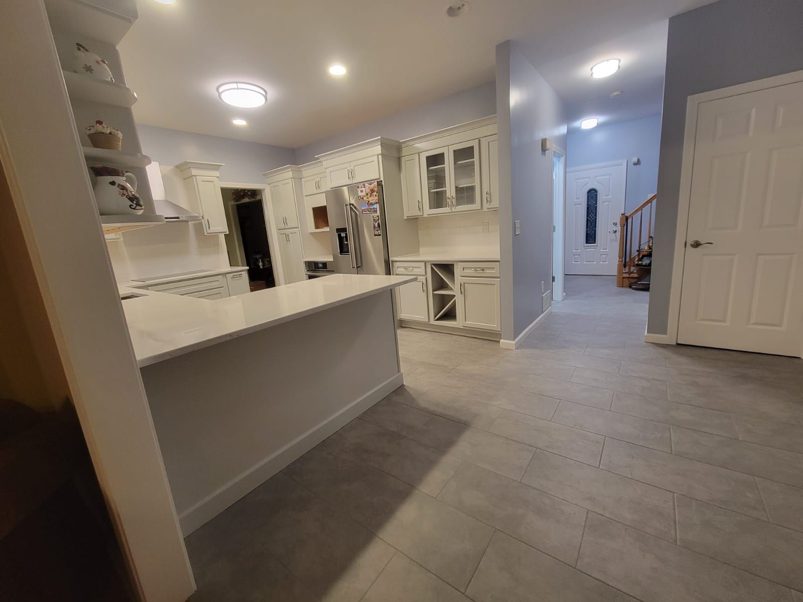 Kitchen with white cabinets, island, and gray tile floor, hallway with front door.