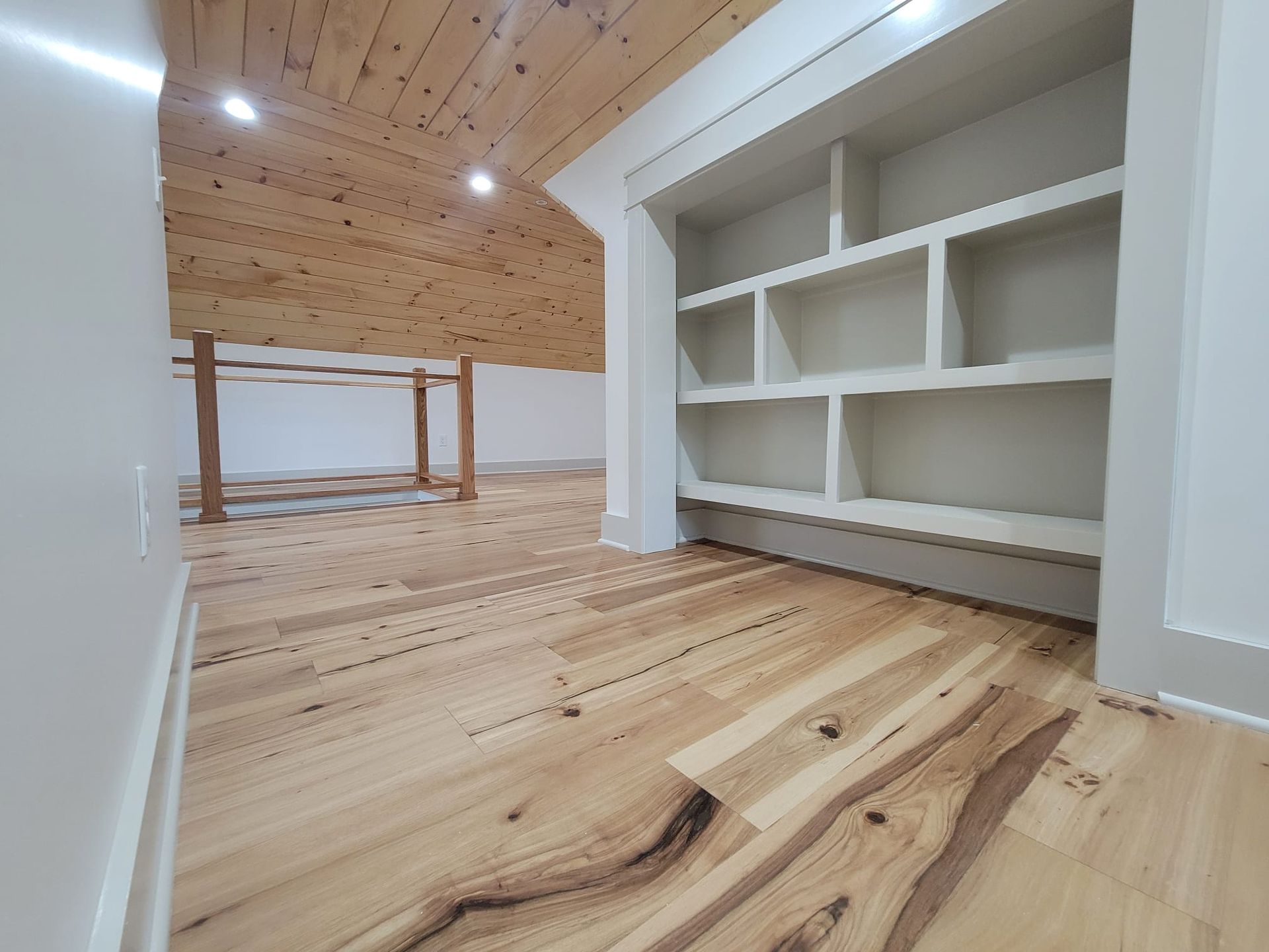 Wooden floors lead to built-in white shelves and a loft area with a light wood ceiling.
