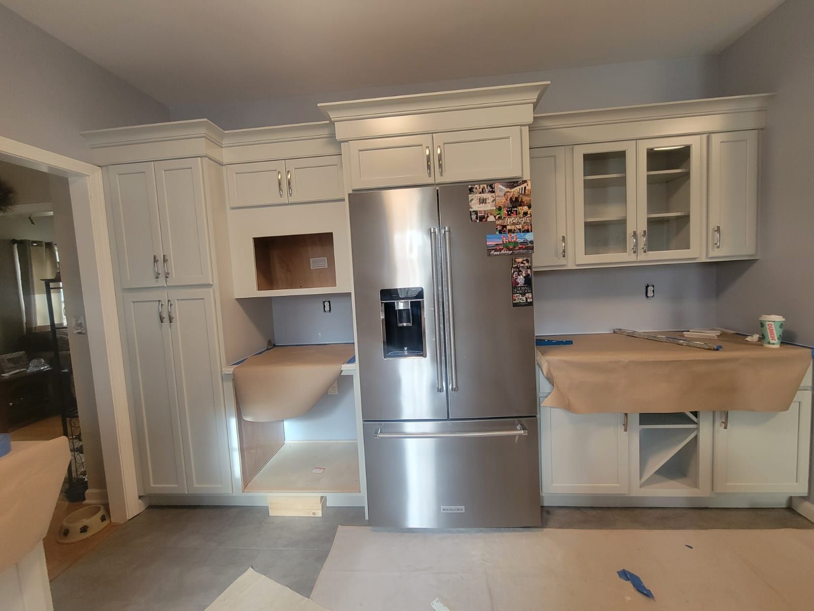 Kitchen with pale grey cabinets, stainless steel fridge, under construction.
