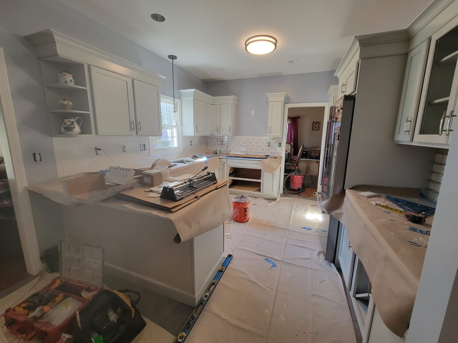 Kitchen remodel: White cabinets, backsplash, tools, and protective coverings on floors and countertops.