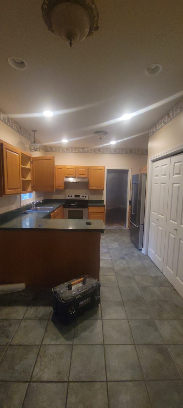 A kitchen with wooden cabinets, a dark countertop, tile flooring, and a toolbox.