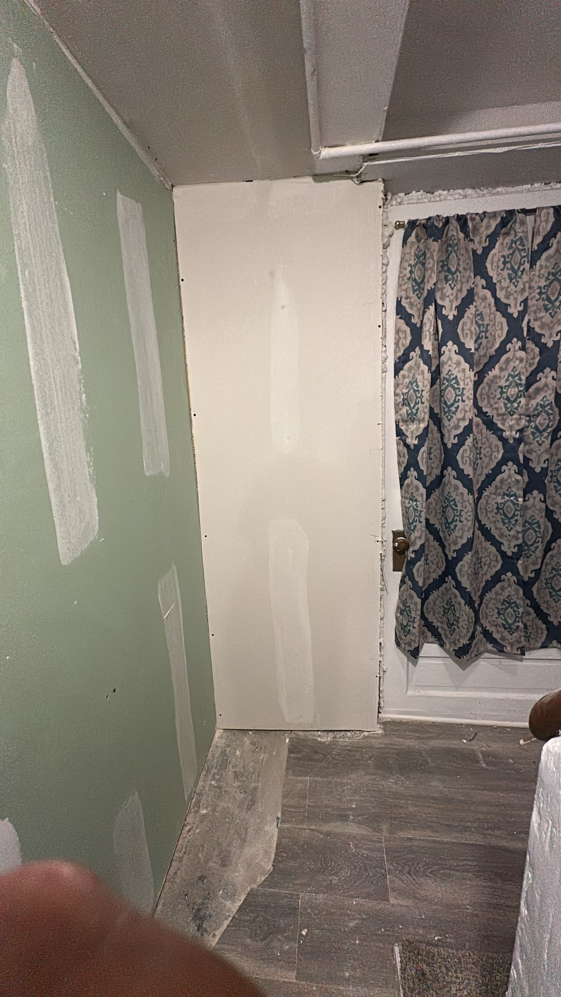Drywall in a room under construction, next to a window with a patterned curtain.