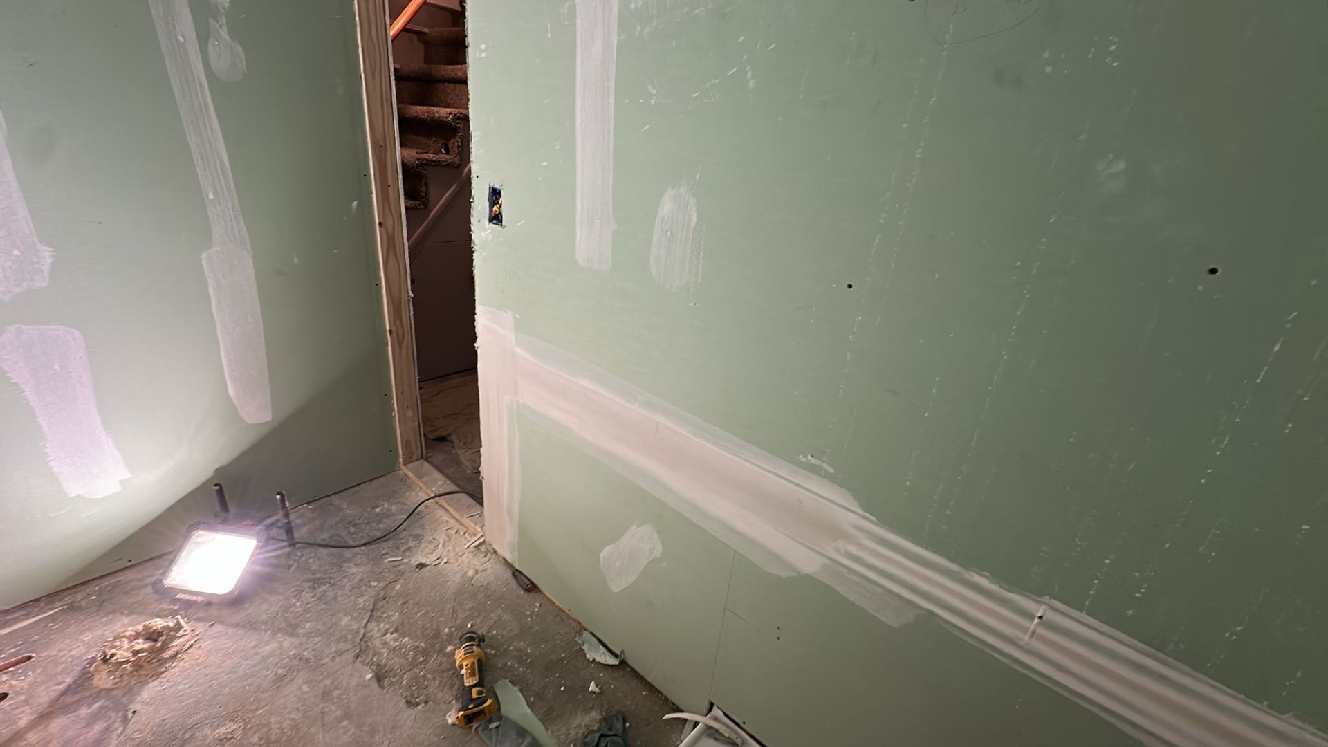 Interior view of unfinished room, walls with green drywall, doorway leads to stairwell.