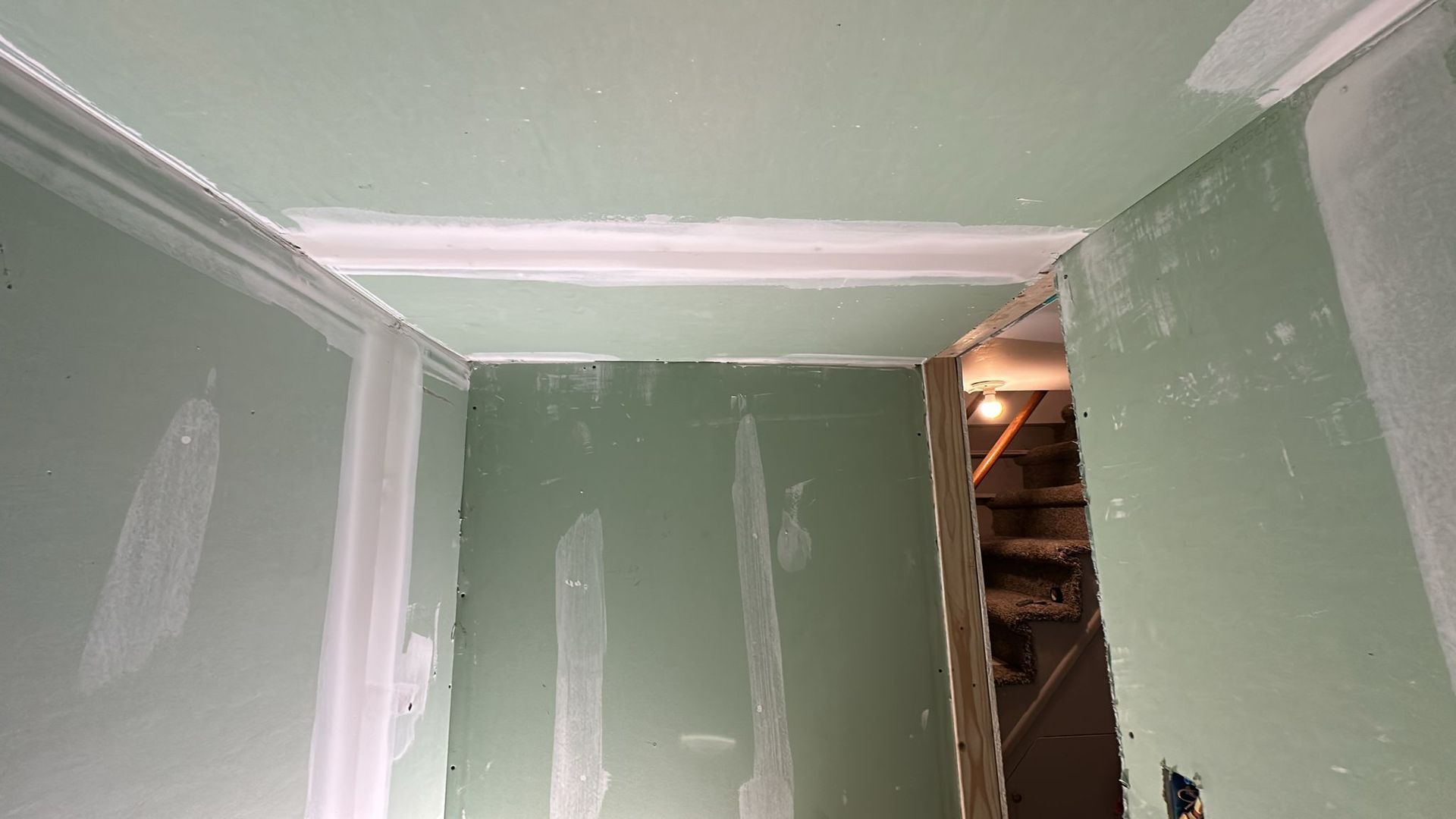 Green drywall hallway with white trim, leading to stairs.