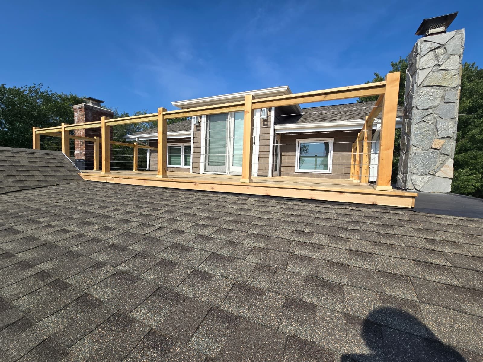 Rooftop wooden deck frame on a house with brown shingles and blue sky.