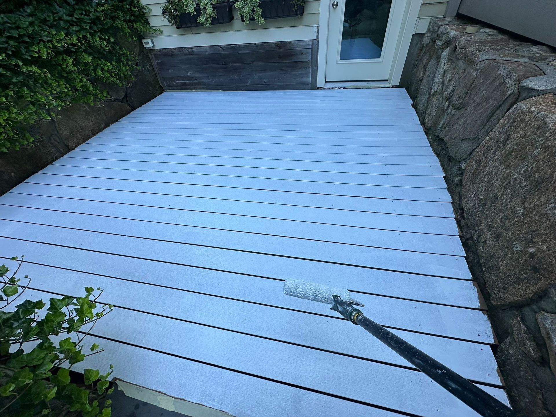 A person painting a light-colored wooden deck with a roller.