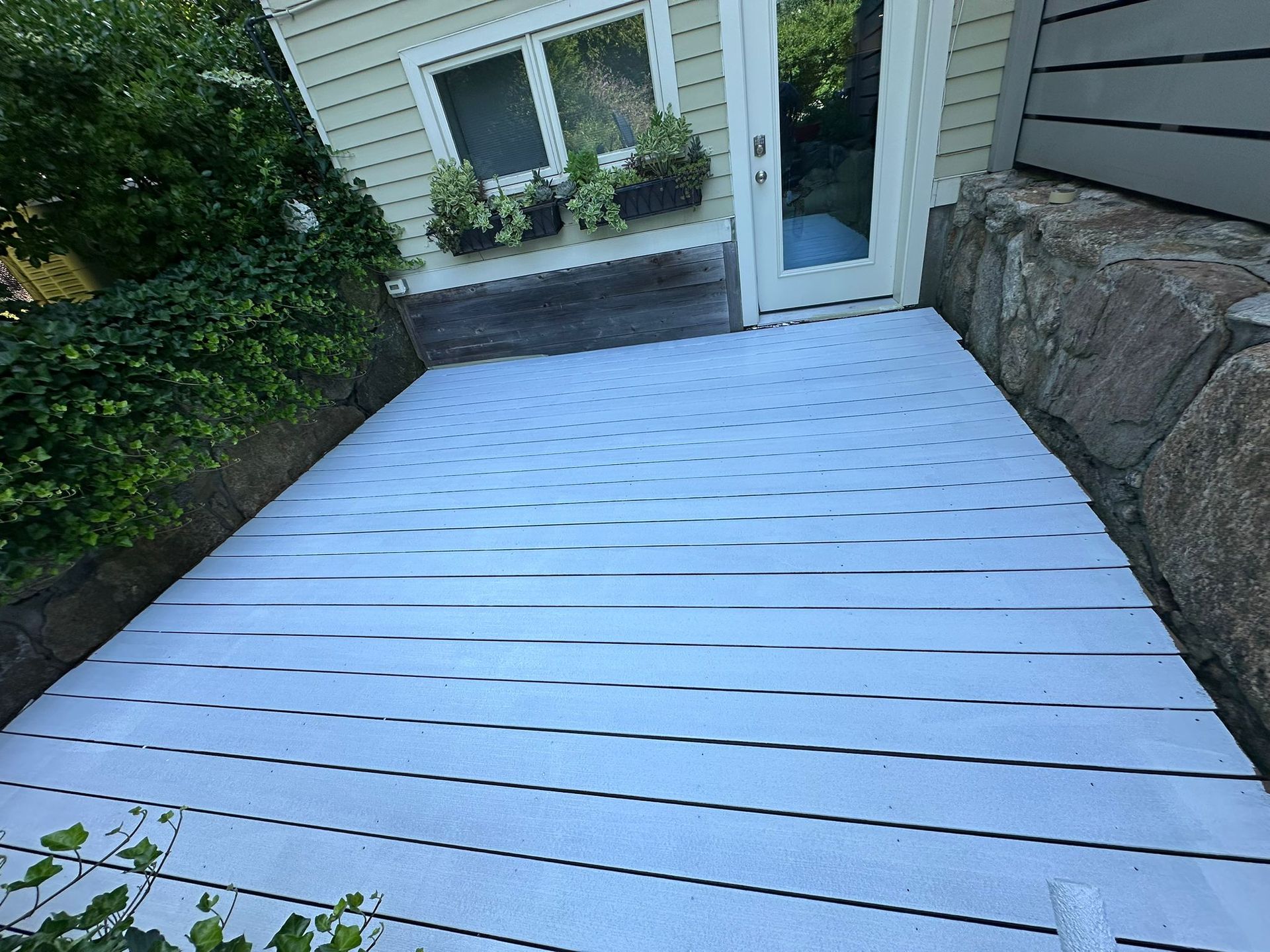 White deck with a doorway, window, and rock wall in the background.