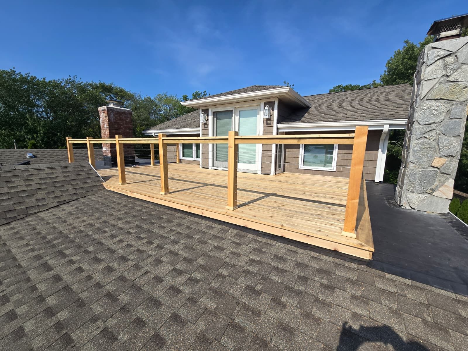Wooden rooftop deck with railing, brown shingles, blue sky.
