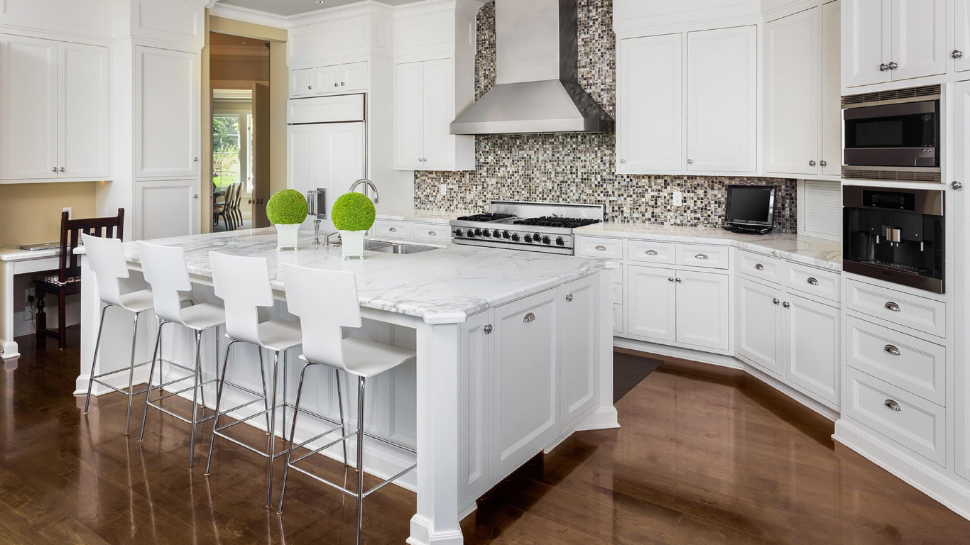 White kitchen with a large island, white cabinets, and stainless steel appliances. Dark wood floor.