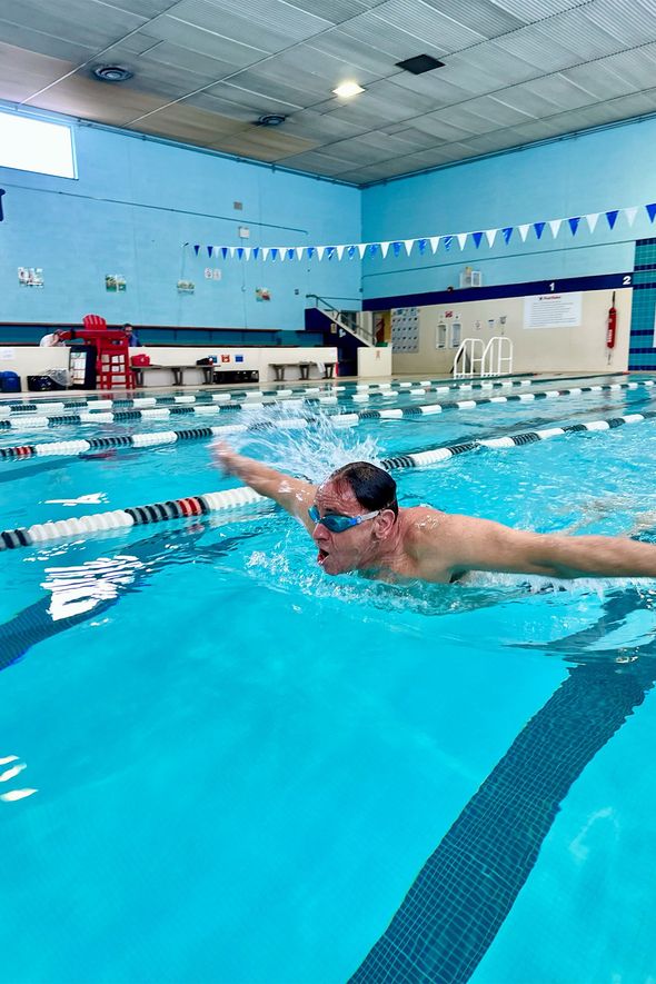 A man is swimming in a large indoor swimming pool.