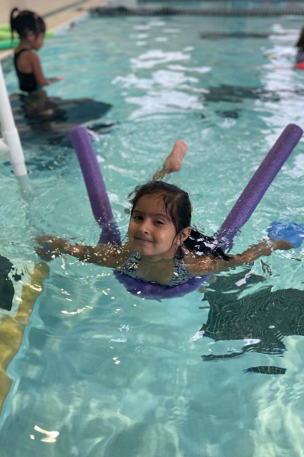 A little girl is swimming in a swimming pool with foam noodles.