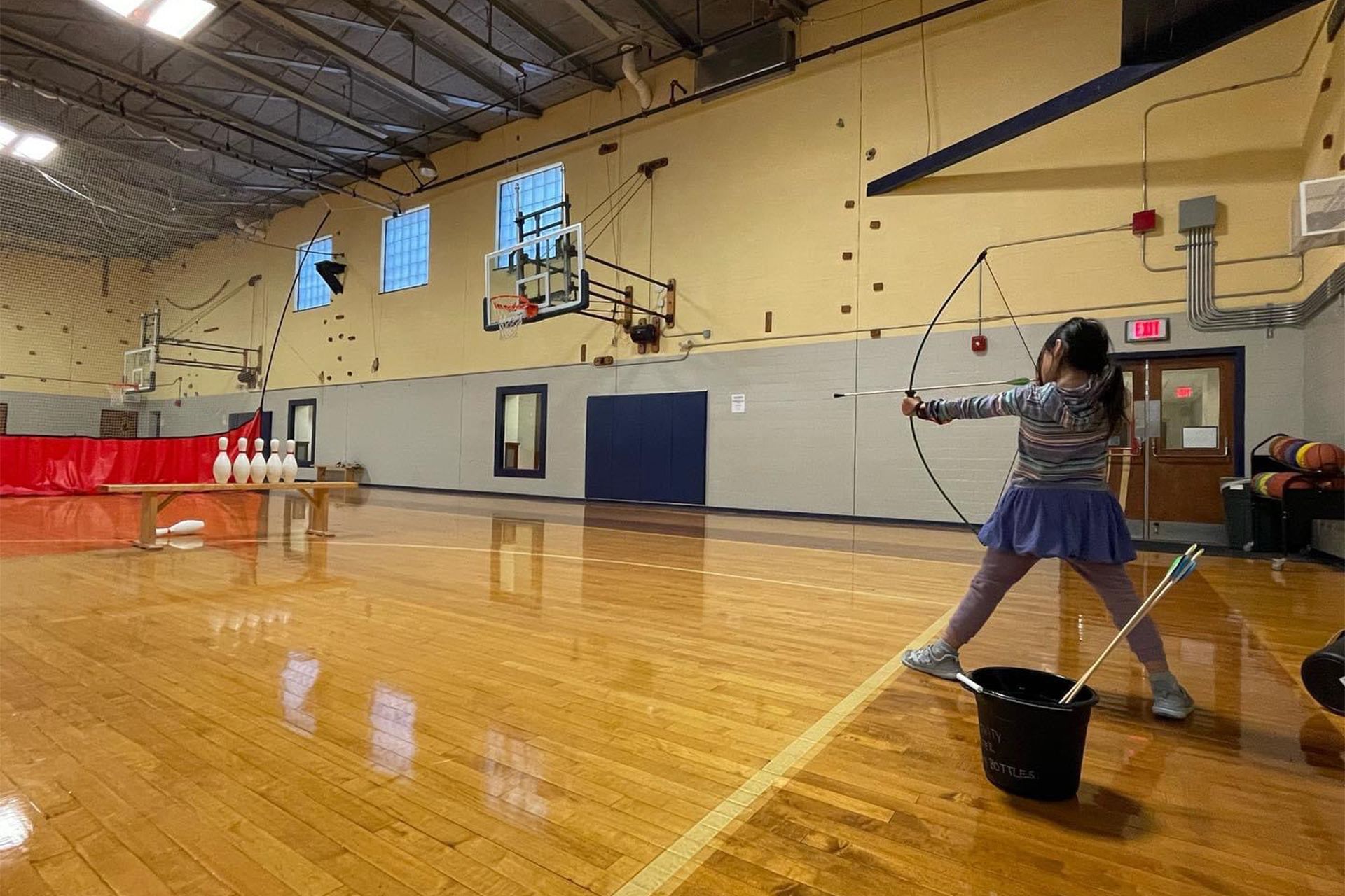 A young girl is practicing archery in a gym.