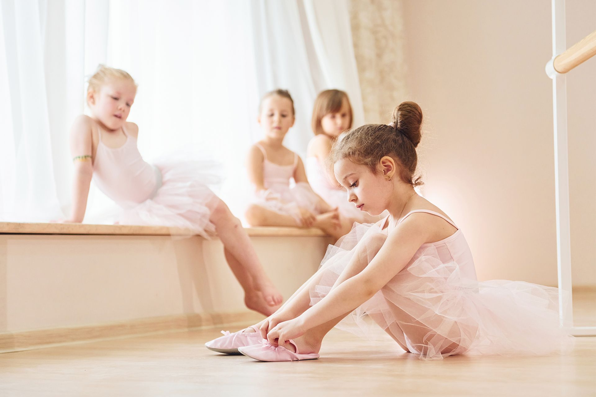 A group of little girls are sitting on a window sill putting on their ballet shoes.