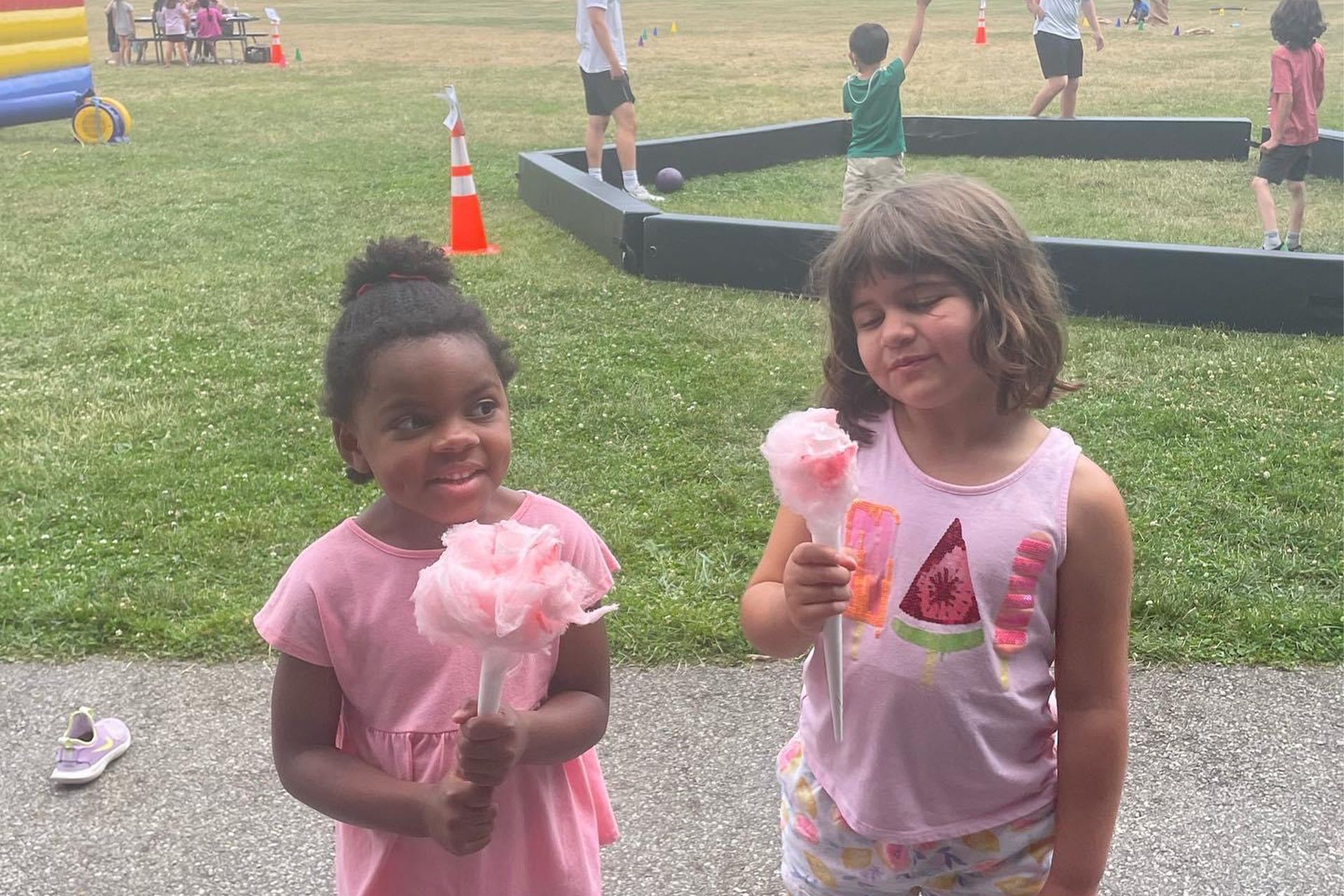 Two little girls are eating cotton candy in a park.