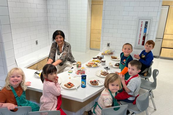 A group of children are sitting around a table with plates of food.