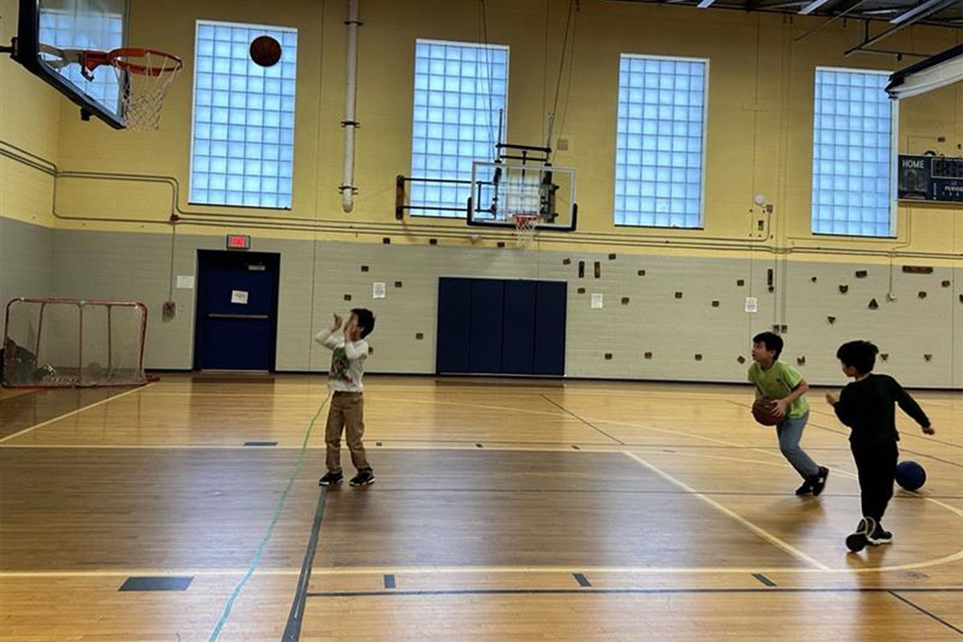Three young boys are playing basketball in a gym.