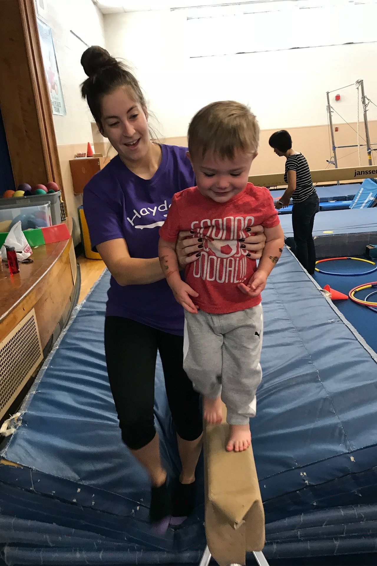 A woman is helping a young boy balance on a balance beam.
