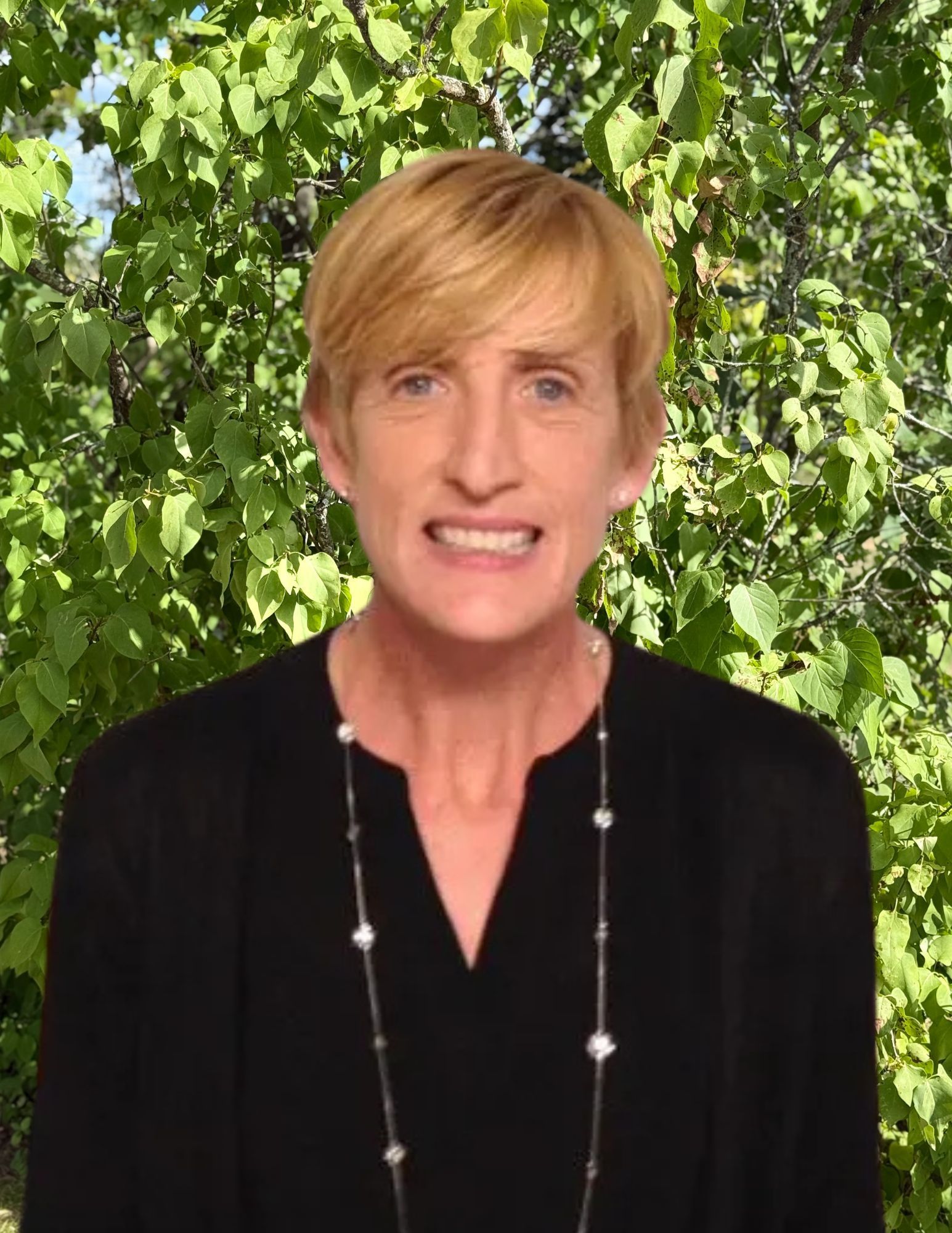 A woman wearing a black shirt and pearl necklace smiles for the camera