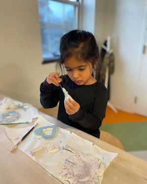 A little girl is sitting at a table decorating cookies.