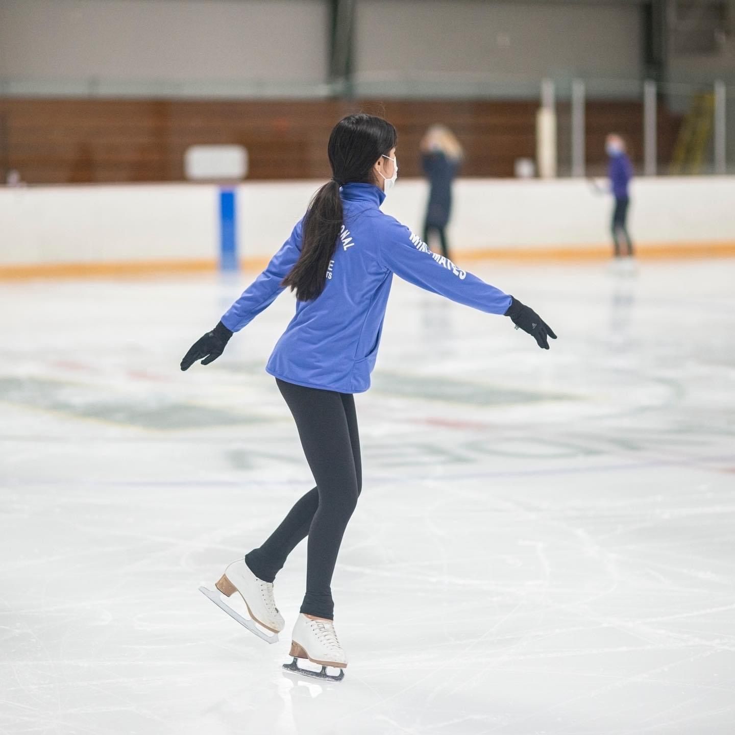 A woman in a blue jacket is ice skating on a rink