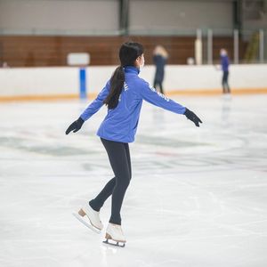 A woman in a blue jacket is ice skating on a rink