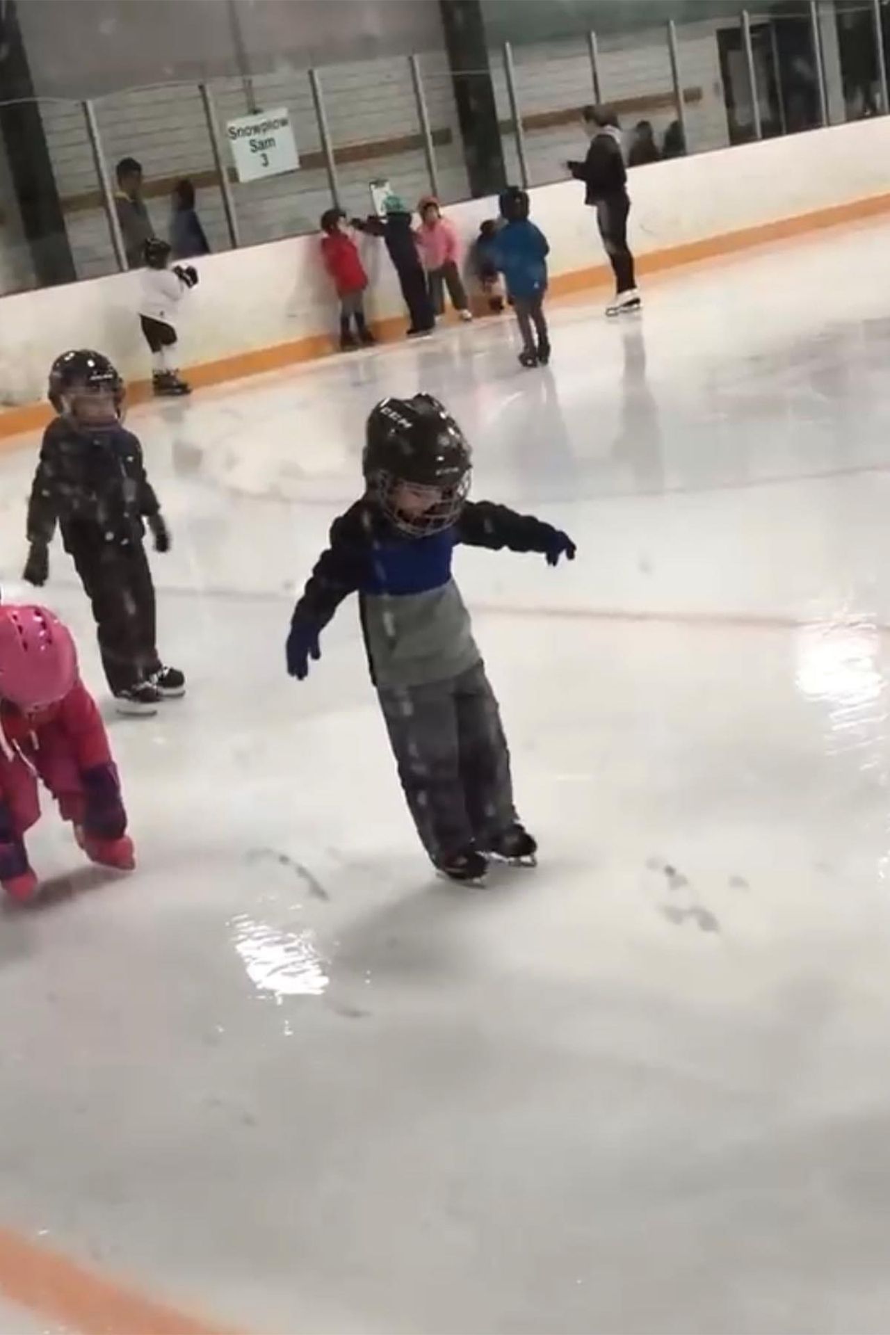 A group of children are ice skating on a rink.