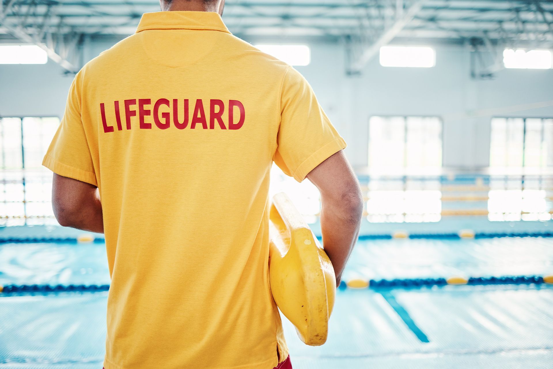 A lifeguard is standing in front of a swimming pool holding a helmet.
