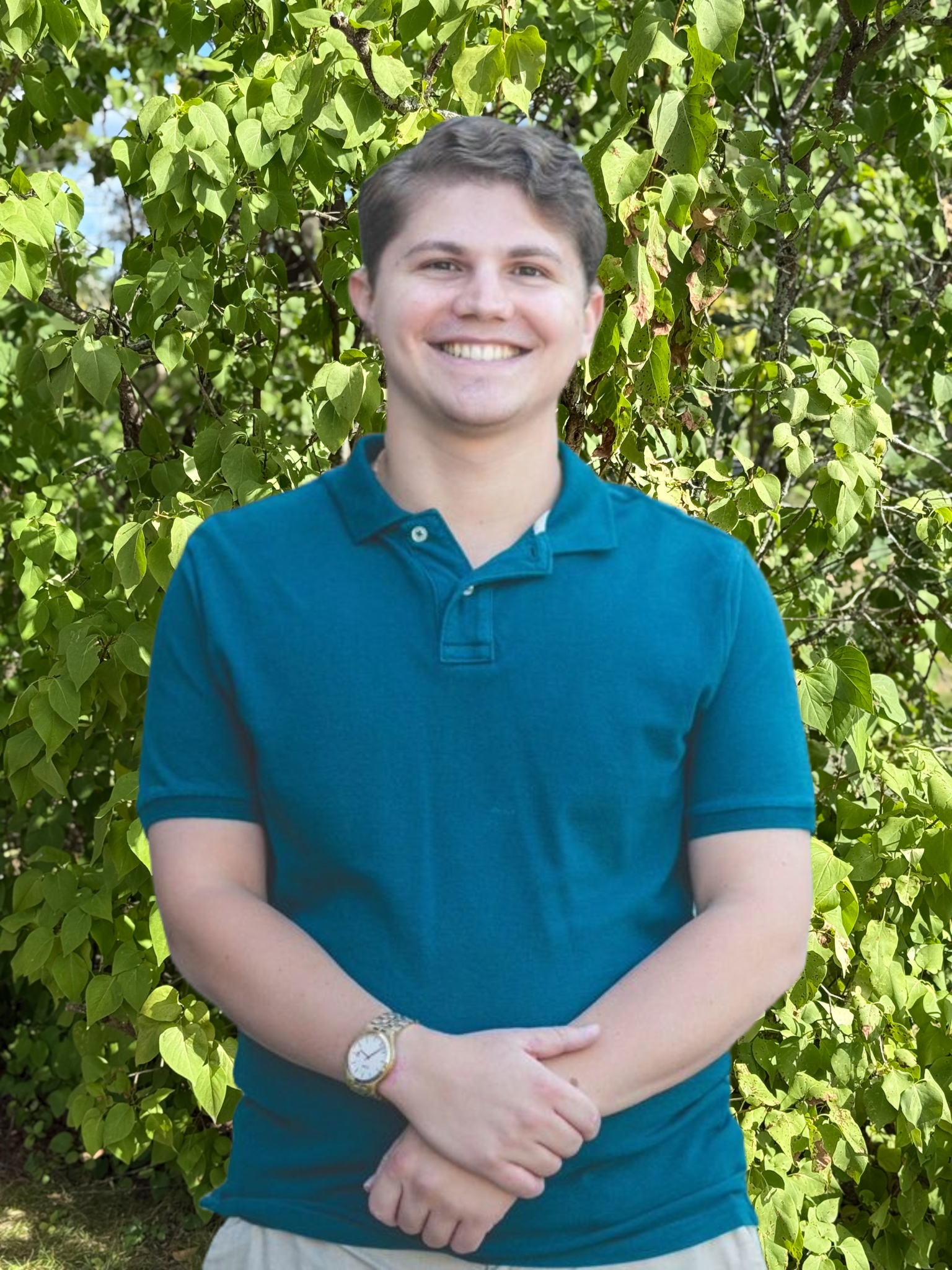 A young man wearing a blue polo shirt and a watch is standing in front of a brick building.