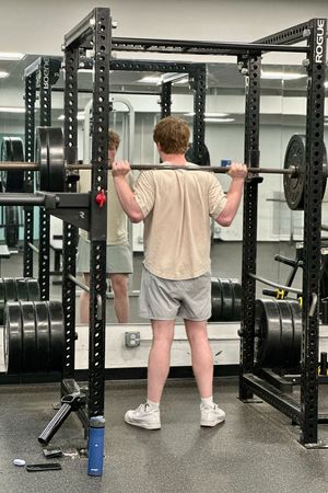 A man is squatting with a barbell in a gym.