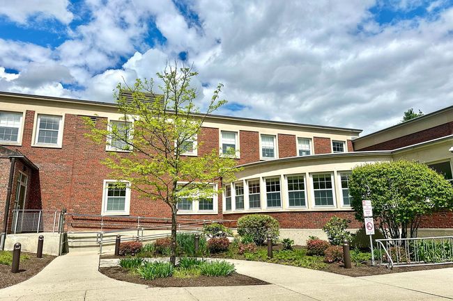 A large brick building with a lot of windows and trees in front of it.