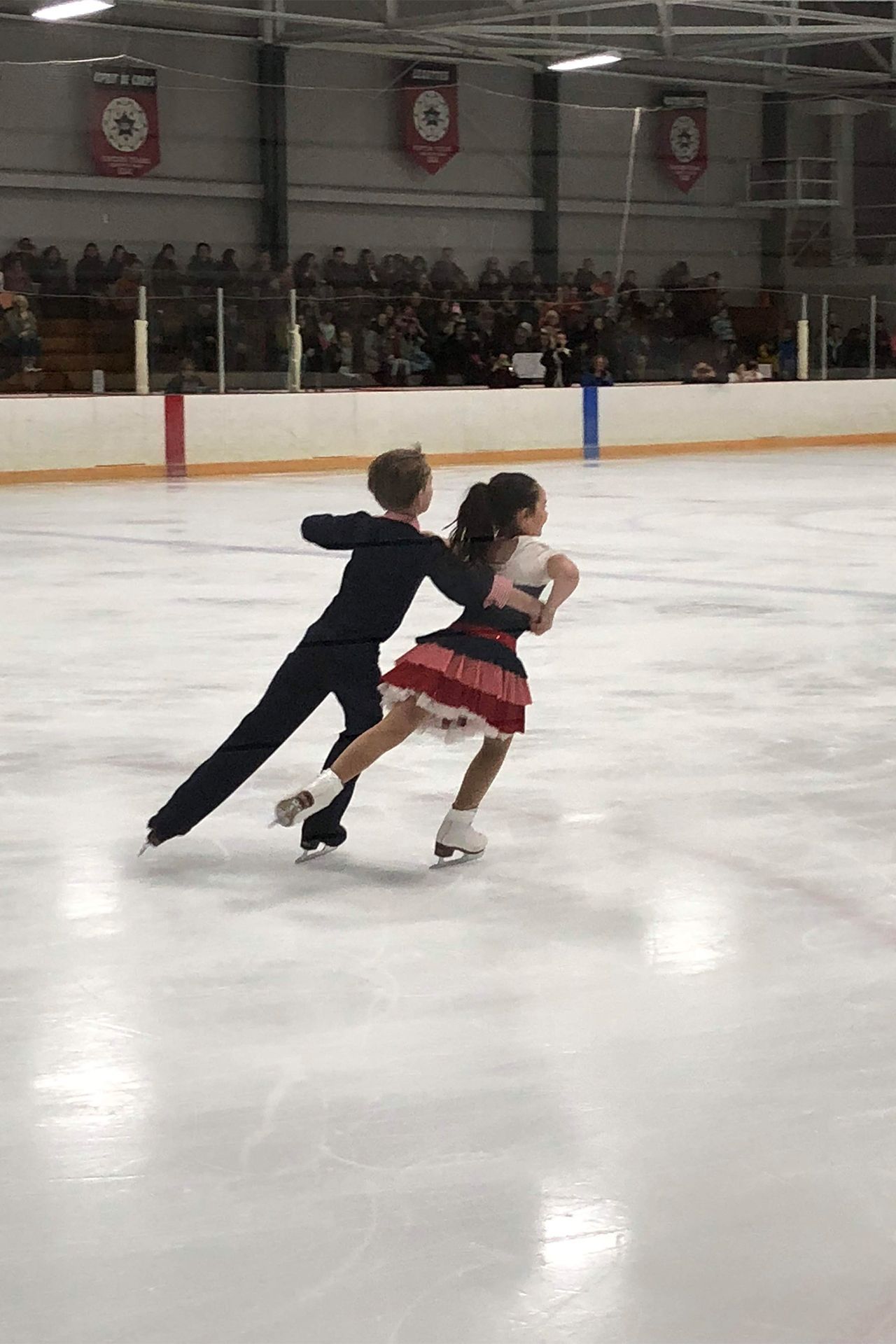 A boy and a girl are ice skating on a rink.