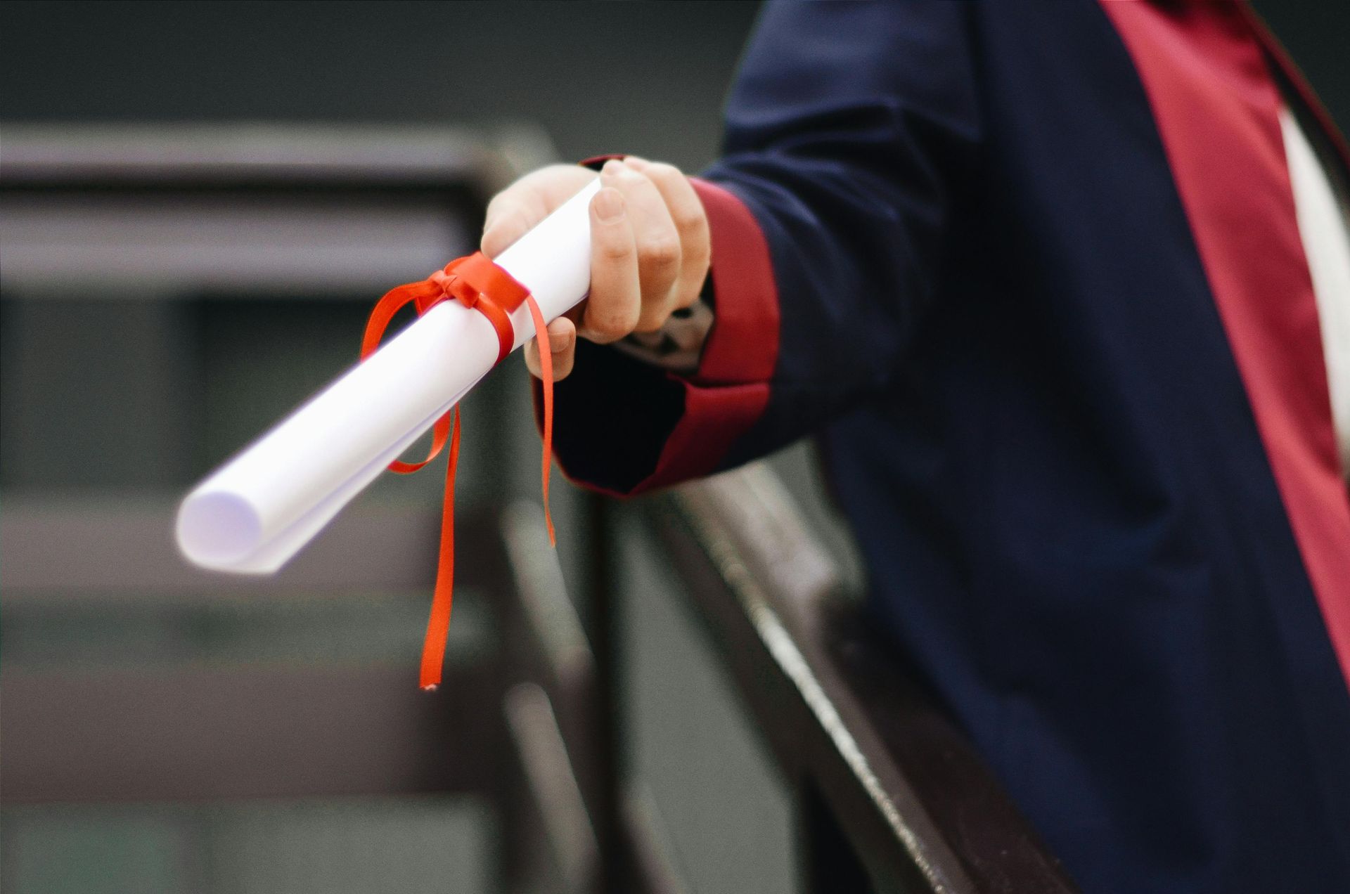 A person is holding a diploma with a red ribbon around it.