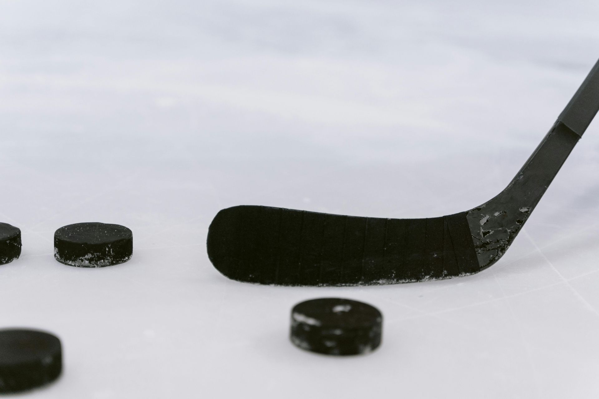 A hockey puck is laying on the ice next to a hockey stick.