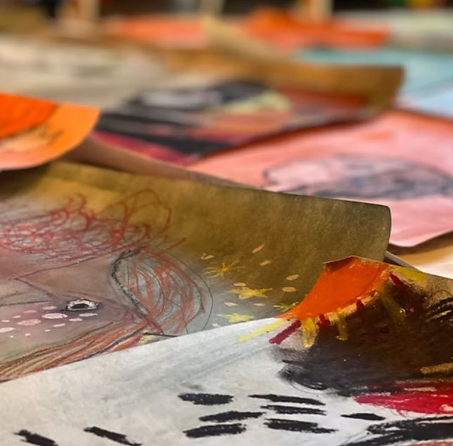 Close-up of colorful drawings on a table. One shows a volcano erupting orange lava, and another a red-haired figure.